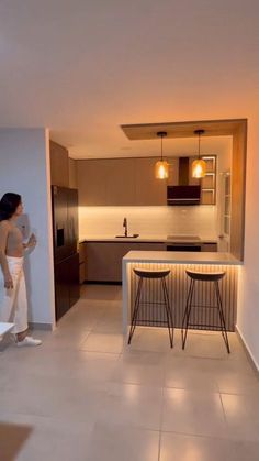 a woman standing in a kitchen next to a table with chairs on it and two stools