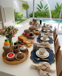 a table set with plates, cups, and utensils in front of a swimming pool