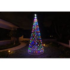 a lighted christmas tree in the middle of a yard at night with lights on it