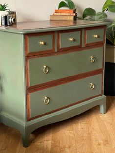 a green dresser with two drawers and some books on top of it next to a potted plant