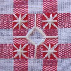 four small white flowers on a red and white checkered table cloth with stitching