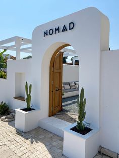 a white building with a wooden door and cactus in the planter next to it