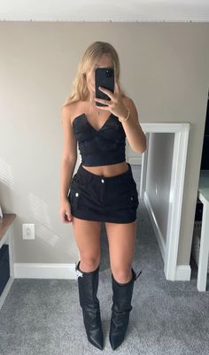 a woman taking a selfie in front of a mirror wearing black shorts and boots