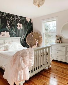 a white bed sitting in a bedroom next to a dresser and window on top of a hard wood floor