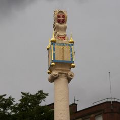 a statue on top of a pole in the middle of a city with dark clouds behind it