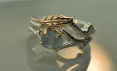 a silver ring with a leaf on it and a stone in the middle, sitting on a table