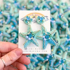 a hand holding up a pair of starfish brooches in blue and green