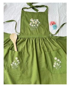 a green apron with daisies on it and a wooden spoon in the pocket next to it