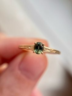 a close up of a person holding a gold ring with a green stone in it