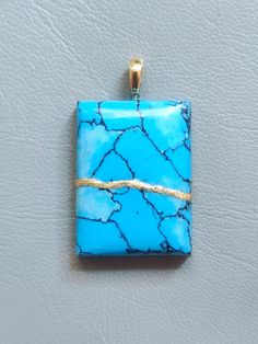 a square pendant with blue marble and gold wire on a white surface, hanging from a hook