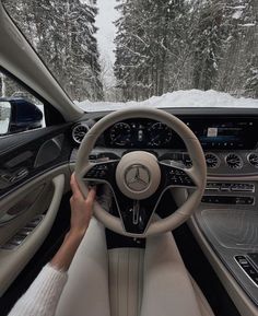 a person driving a car on a snowy road with snow covered trees in the background