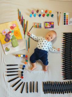 a baby laying on top of a table with lots of art supplies next to it