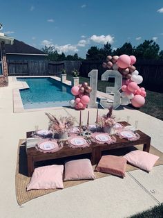 a table set up with pink and white balloons in front of a pool for a birthday party