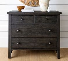 a black dresser with two drawers and a basket on top of it next to a white wall