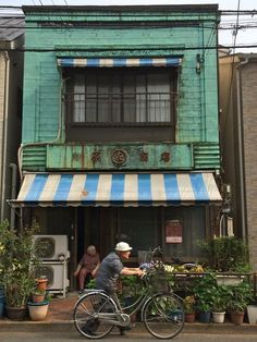 a man riding a bike past a green building with blue and white awnings