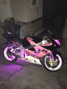 a pink and black motorcycle parked in front of a building with purple lights on it