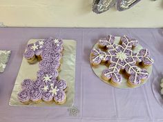 purple frosted cupcakes and cookies are displayed on a table with silver plates