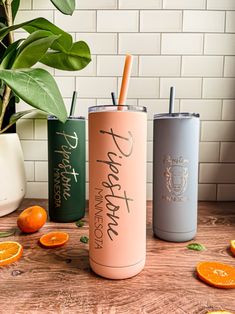 three different colored tumblers sitting on top of a wooden table next to oranges