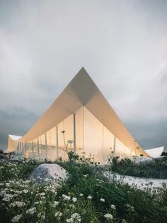 the building is made out of glass and has white flowers growing in front of it