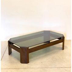 a coffee table with glass top and wooden frame on the bottom, in front of a white wall