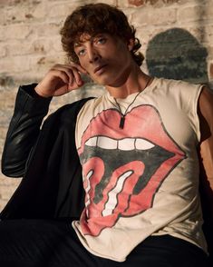 a young man sitting in front of a brick wall wearing a rolling stones t - shirt