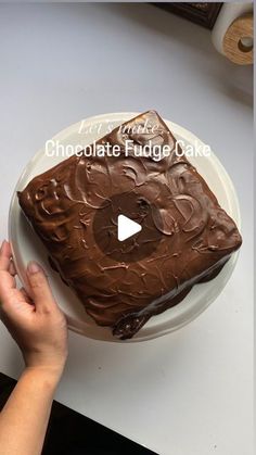 someone is cutting into a chocolate fudge cake on a white plate with the words, chocolate fudge cake