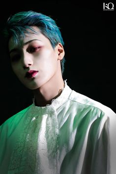 a man with blue hair wearing a white shirt and green collared shirt in the dark