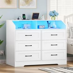 a white dresser with two blue drawers in a room next to a bed and plants