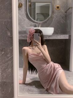 a woman in a pink dress taking a selfie with her cell phone while sitting on the floor