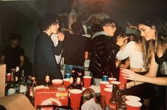 a group of people standing around a table filled with cups and drinks at a party