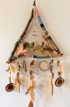 a triangle shaped wall hanging with feathers, beads and other things on it's side