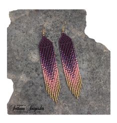 pink and purple beaded earrings sitting on top of a gray stone slab next to a rock