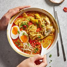 two hands holding a bowl of noodles and eggs