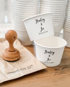 two cups and a rubber stamp sitting on top of a wooden table next to white plates