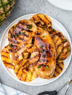 grilled chicken with pineapple sauce on a white plate next to sliced pineapples