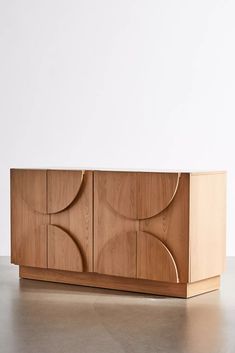 a wooden cabinet sitting on top of a floor next to a white wall with an abstract design