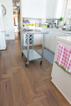 a kitchen with white cabinets and wood flooring on the walls, along with an island cart