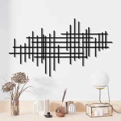 a wall sculpture made out of black sticks on a white wall next to vases