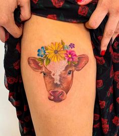 a woman's thigh with a tattoo of a cow wearing a flower crown on it