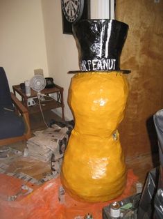 a large yellow vase with a black top hat on it's head sitting in front of a wall