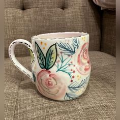 a coffee cup with flowers painted on it sitting on a couch next to a pillow