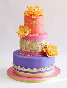 a three tiered cake with flowers on top and gold trimming around the edges