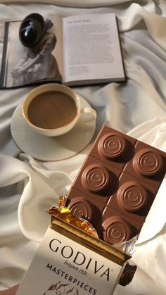 a cup of coffee and some kind of chocolate bar on a bed with an open book