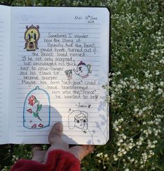 someone holding up a book with drawings on it in front of some plants and flowers