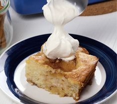 a piece of cake on a blue and white plate with whipped cream being drizzled over it