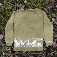 a green sweater with white snowflakes is laying on the ground next to grass