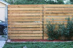 a wooden fence that is next to a car in the yard with grass and bushes