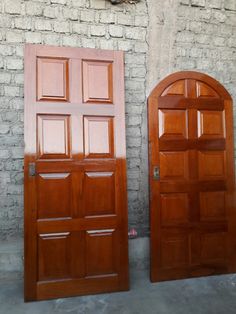 two wooden doors sitting next to each other in front of a brick wall with an arched window