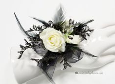 a white rose and black ribbon boutonniere on a napkin holder with feathers