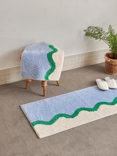 a bathroom rug with green and blue waves on it next to a potted plant